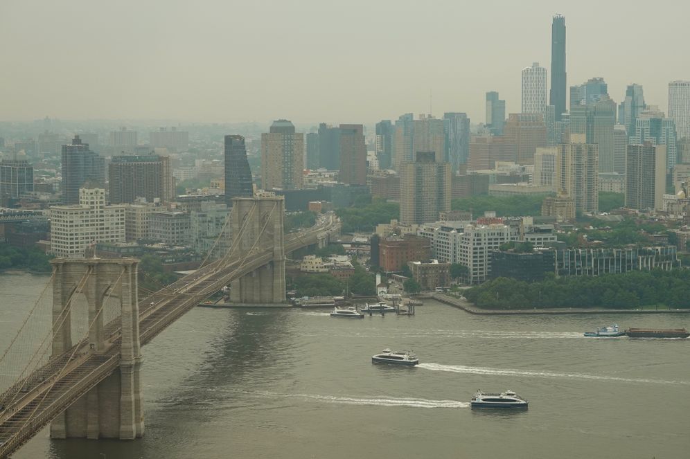 Boats maneuver the East River near the Brooklyn Bridge as smoke from wildfires blankets the sky Thursday, July 16, 2026, in New York. 
