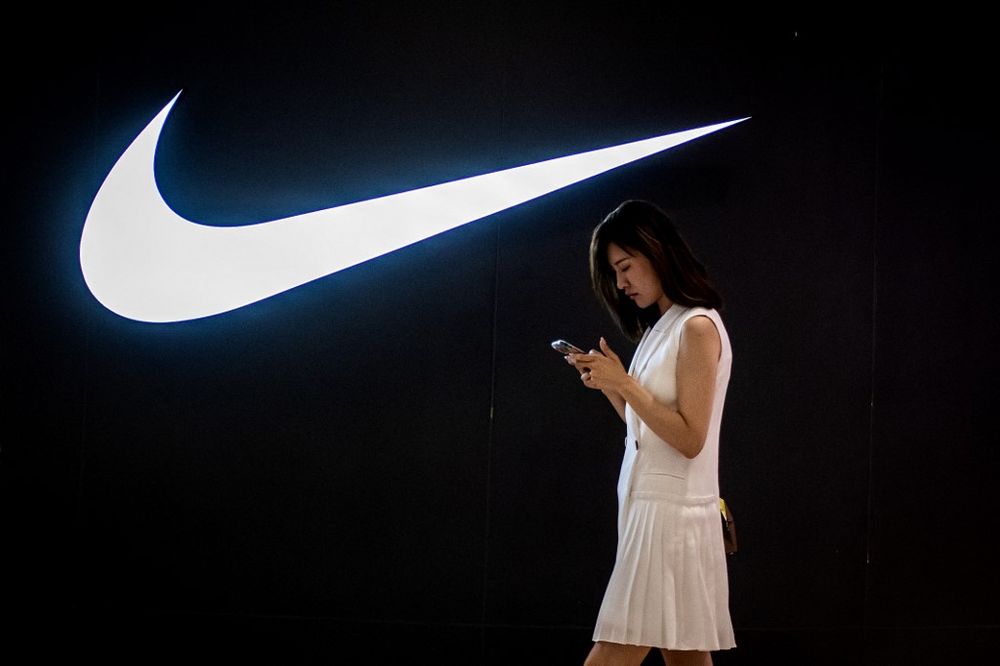 A woman browses her phone while walking past a Nike logo inside a shopping mall in Beijing, China, on June 2, 2021.