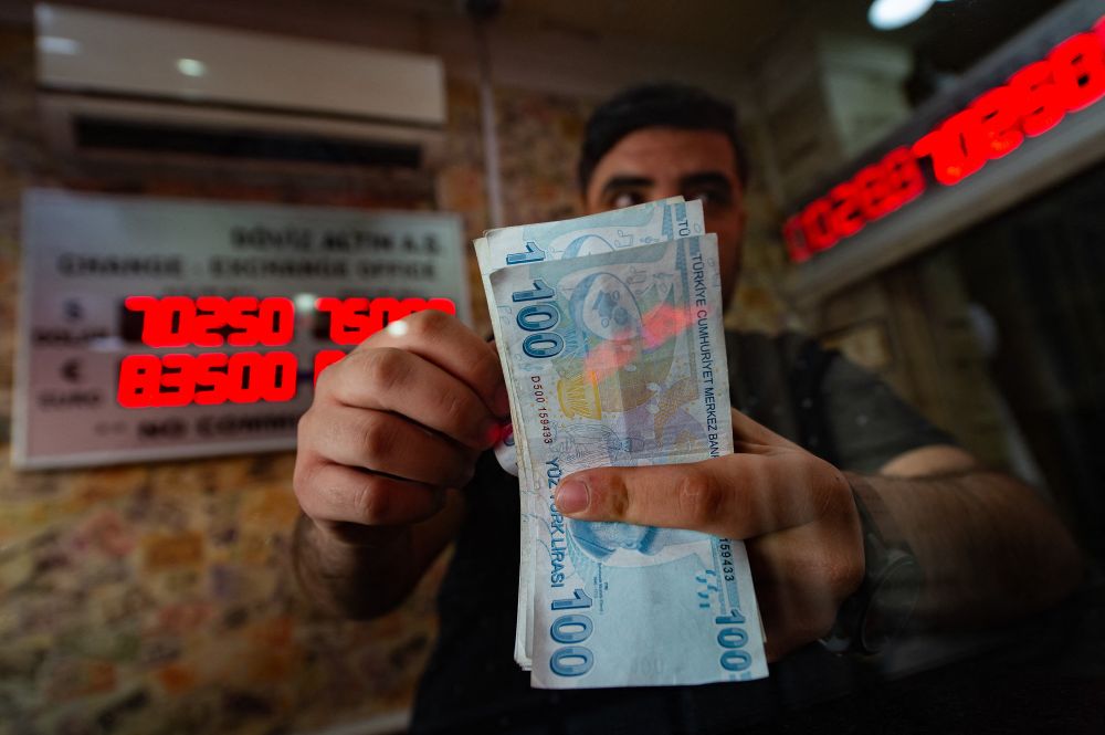 A currency exchange office worker counts Turkish Lira banknotes in front of the electronic panel displaying currency exchange rates at an exchange office in Istanbul, Turkey, August 6, 2020.
