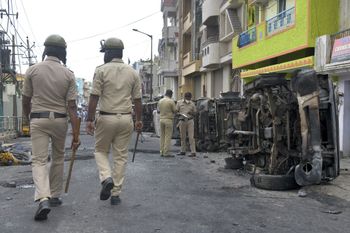 Policemen stand guard next to burnt police vehicles along a street in Bangalore on August 12, 2020, after violence broke out overnight in Devara Jevana Halli area following a "derogatory" Facebook post about the Prophet Mohammed that sparked riots.