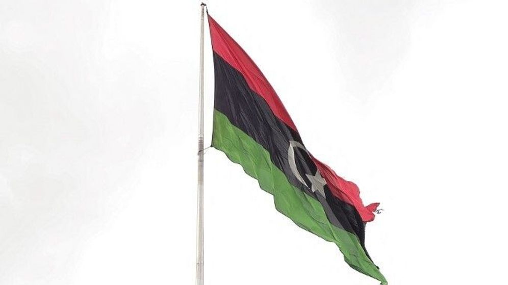 يرفرف علم وطني ليبي كبير فوق عمال النظافة الذين يتفقدون العشب بحثاً عن الأعشاب الضارة في حديقة عامة بالعاصمة الليبية طرابلس في 22 أبريل 2024.