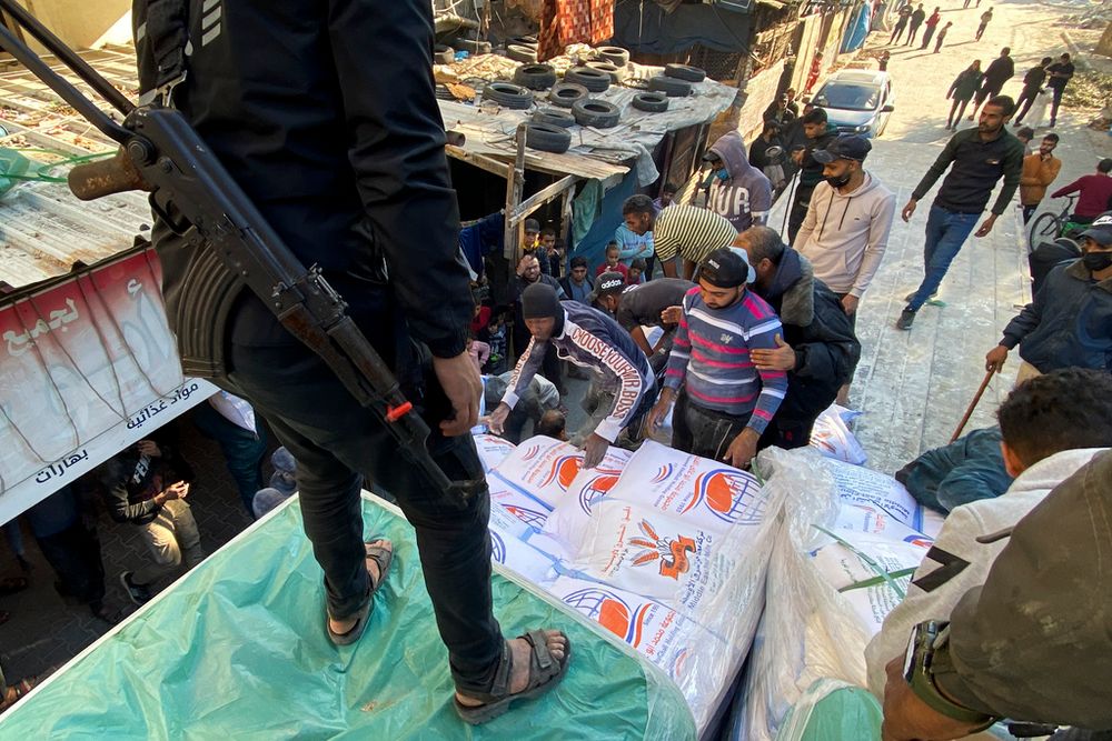 Palestinians unload bags of wheat from a humanitarian aid truck at a grocery store guarded by Hamas fighters in Rafah, Gaza Strip