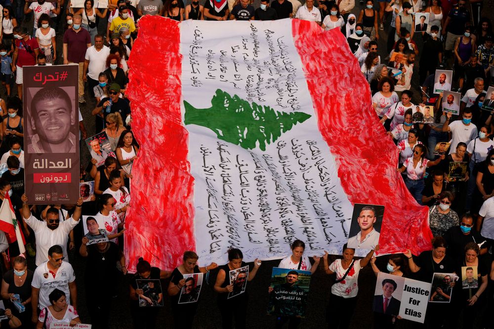 Relatives of victims of the deadly 2020 Beirut port explosion hold portraits of loved ones and an altered Lebanese flag to mark the second anniversary of the massive blast, outside the port of Beirut, Lebanon, on August 4, 2022.