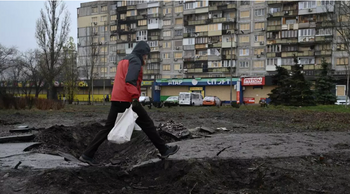 Un homme marche sur un cratère devant un immeuble résidentiel endommagé après une récente attaque aérienne, à Kiev, le 3 décembre 2025 
