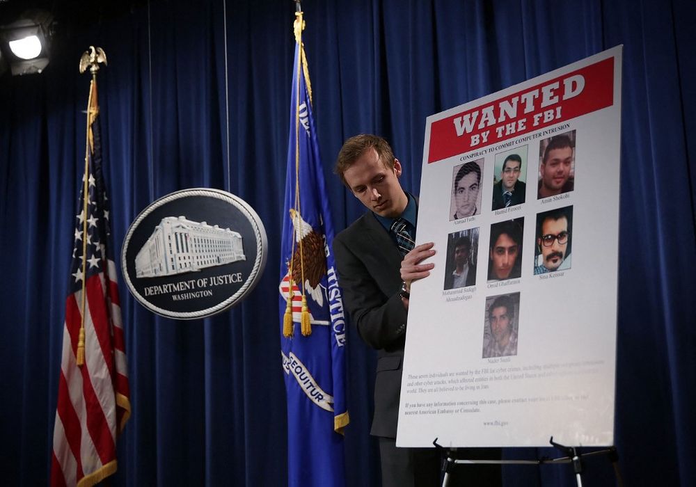 A Department of Justice employee puts up a poster of seven indicted hackers prior to a news conference March 24, 2016 in Washington, DC, USA.