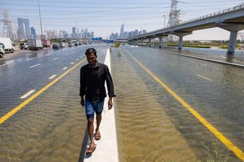 A man walks along a road barrier among floodwater caused by heavy rain on Sheikh Zayed Road highway in Dubai, United Arab Emirates, April 18, 2024.