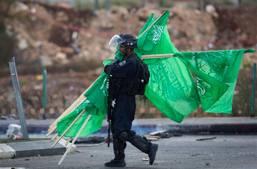 A member of the Israeli security forces carries flags of Hamas found near Ramallah, the West Bank, on October 8, 2015.