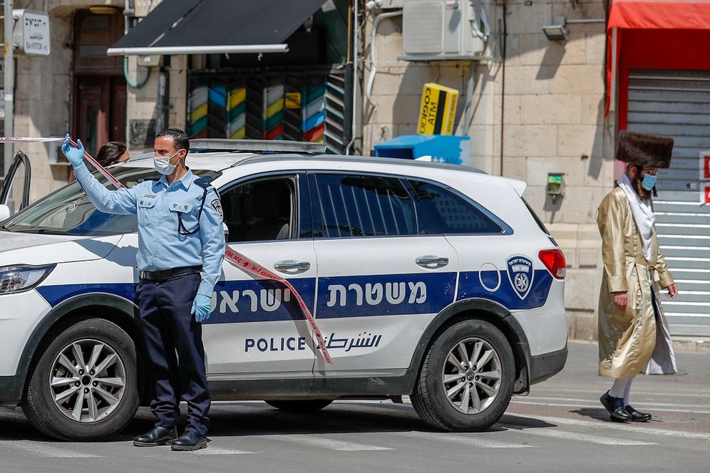 An ultra-Orthodox Jewish man walks past an Israeli police car, stationed at the entrance of the Mea Shearim neighborhood in Jerusalem on April 12, 2020, during the novel coronavirus pandemic
