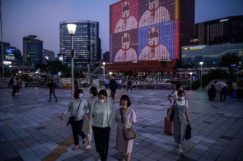 People walk below a display on a building showing messages of support for health workers and the country amid the COVID-19 coronavirus pandemic outside Seoul station on July 8, 2020.
