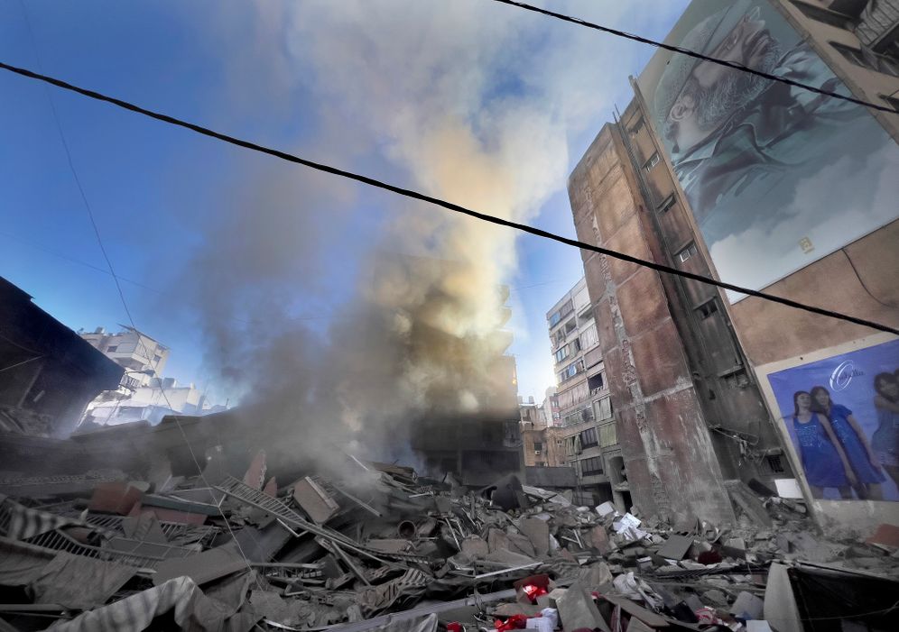 Smoke rises near a giant portrait of the late Hezbollah military commander Imad Mughniyeh from a destroyed building that was hit by an Israeli airstrike in Dahieh
