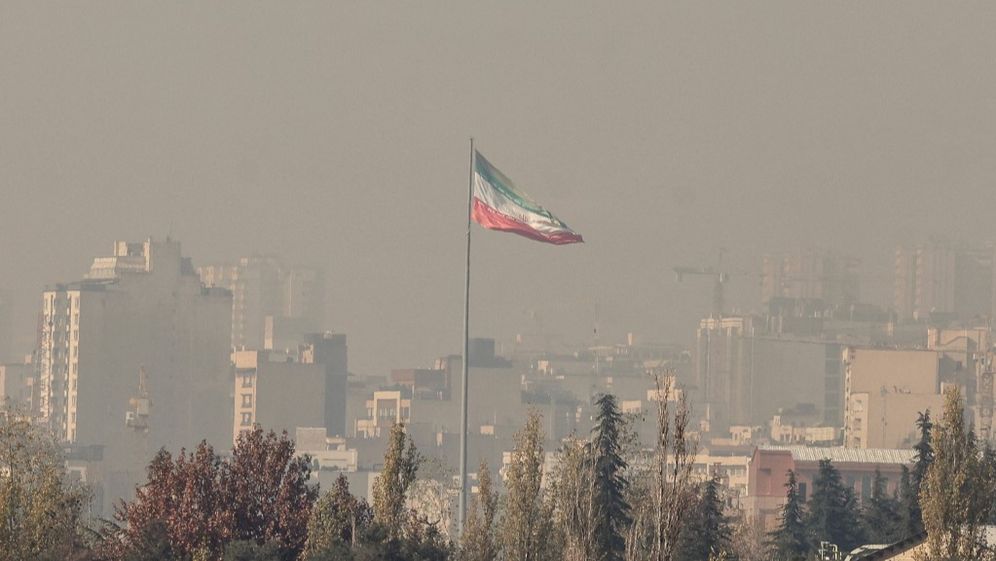 The Iranian flag flies over Tehran, shrouded in thick smog, on November 25, 2025.