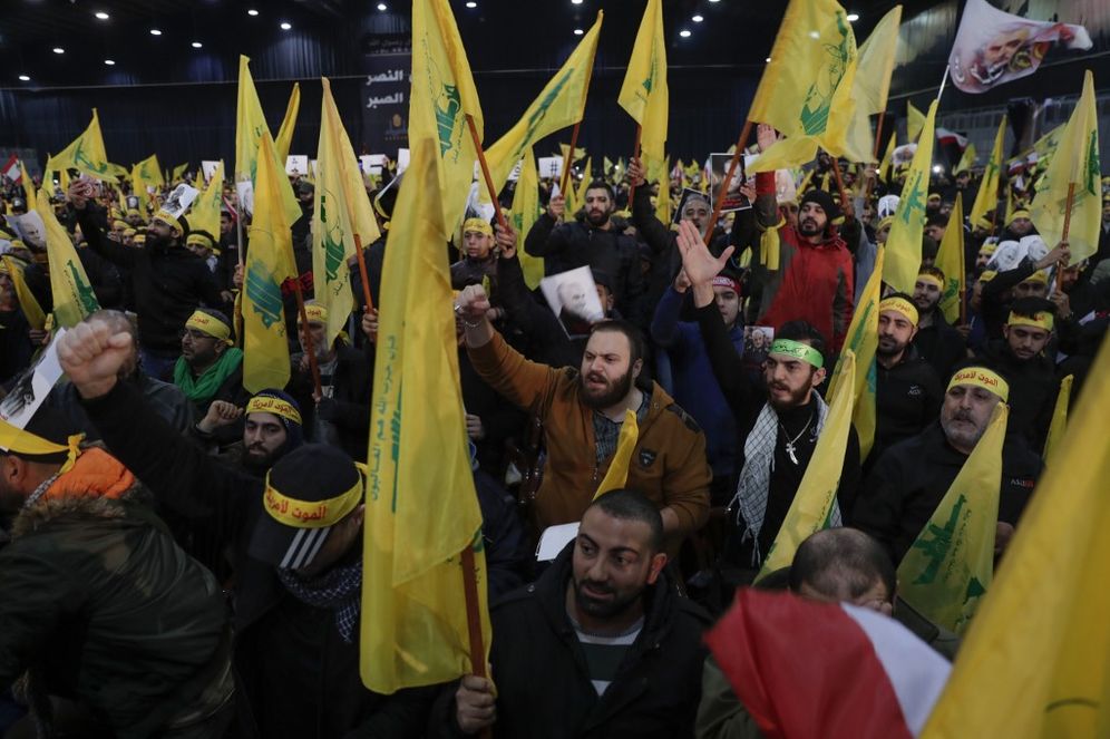 Supporters of the Shiite Hezbollah movement wave flags as the movement's leader delivers a speech on a screen in the Lebanese capital Beirut's southern suburbs on January 5, 2020.