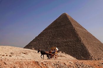 مصريون يركبون عربة أمام هرم خوفو، في الخلفية، بالقرب من القاهرة، مصر