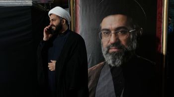 A cleric speaks on his cellphone next to a portrait of Iran's Supreme Leader Ayatollah Mojtaba Khamenei during a pro-government gathering near the residence where his father, former Supreme Leader Ayatollah Ali Khamenei, was killed during U.S. and Israeli strikes on Feb. 28, in Tehran, Iran, Monday, May 18, 2026. 