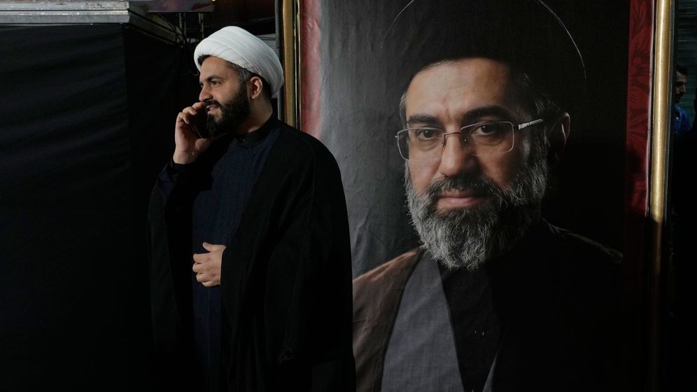 A cleric speaks on his cellphone next to a portrait of Iran's Supreme Leader Ayatollah Mojtaba Khamenei during a pro-government gathering near the residence where his father, former Supreme Leader Ayatollah Ali Khamenei, was killed during U.S. and Israeli strikes on Feb. 28, in Tehran, Iran, Monday, May 18, 2026. 