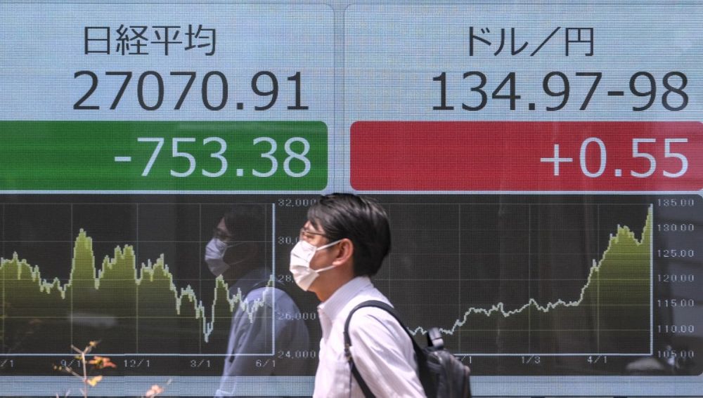 A pedestrian walks past an electronic share price board showing the closing numbers on the Tokyo Stock Exchange (L) and a foreign exchange board showing the yen's rate against the US dollar (R) in Tokyo on June 13, 2022.