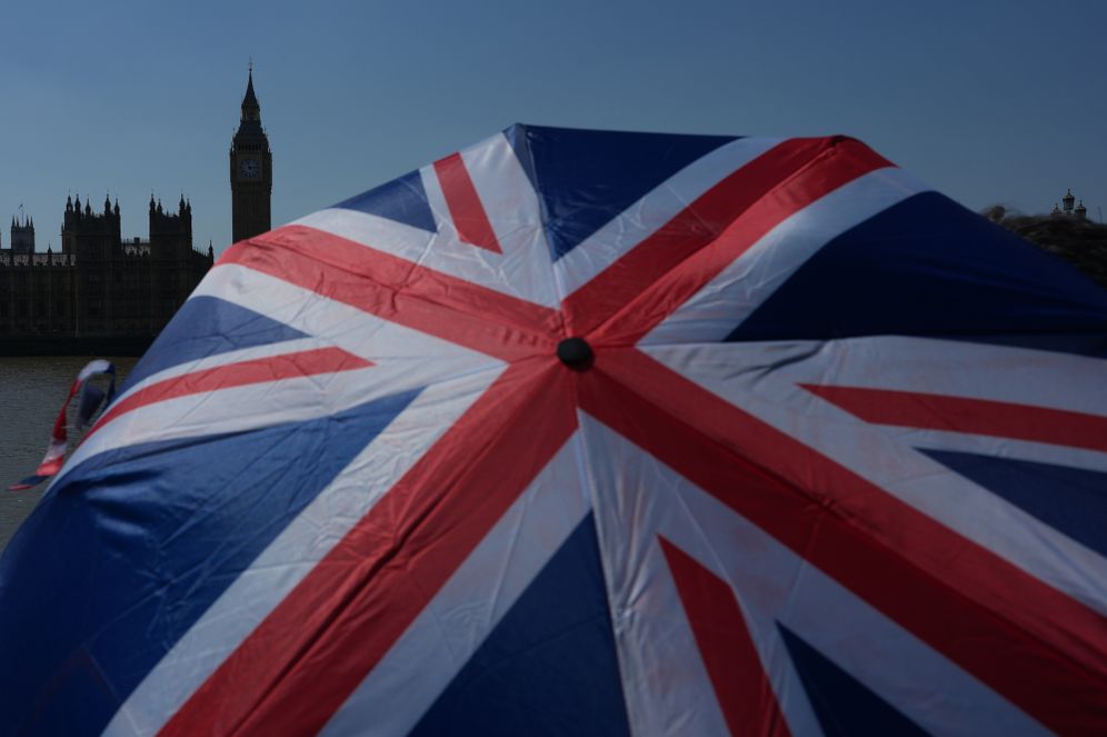 AP Photo/Alastair Grant A tourist poses for a photo holding an umbrella with the British flag over Westminster Bridge towards the Elizabeth Tower, which hold the bell known as 'Big Ben', in London, Wednesday, June 24, 2026.