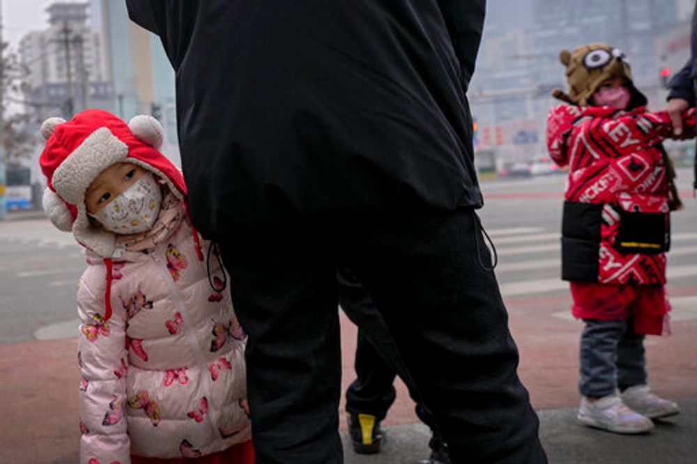 Children stand with relatives waiting to cross a traffic intersection in the Central Business District of Beijing, China, January 24, 2022.