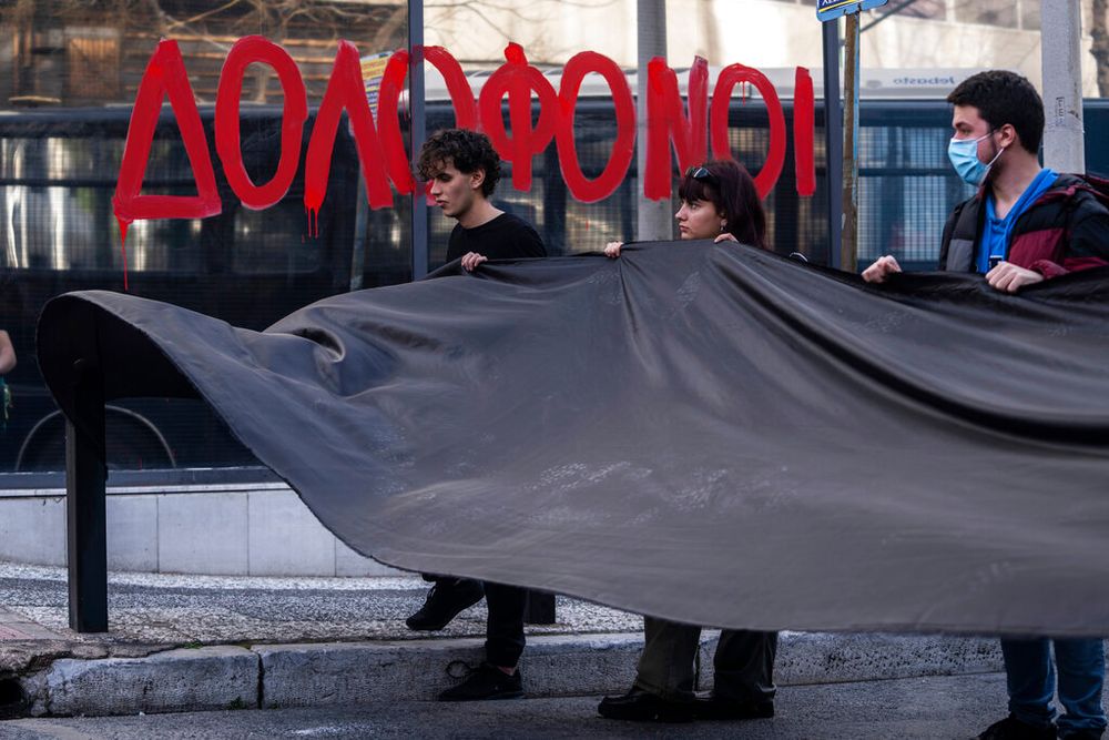 Students hold a black banner walk past a glass painted with the Greek word 'murderers' as they protest outside the headquarters of private operator Hellenic Train, in Athens, Greece.