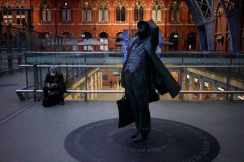 A man wearing a face mask to curb the spread of Covid sits down near the Sir John Betjeman Statue in St. Pancras train station, London, England, January 21, 2022.