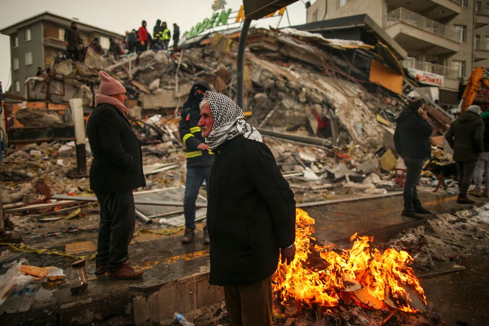 People warm themselves next to a collapsed building in Malatya, Turkey.