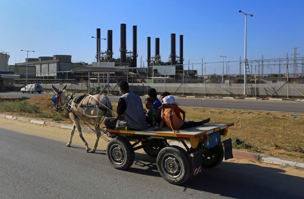أب وأطفاله يركبون عربتهم التي تجرها جمار أمام محطة كهرباء غزة المتوقفة عن العمل في النصيرات وسط قطاع غزة