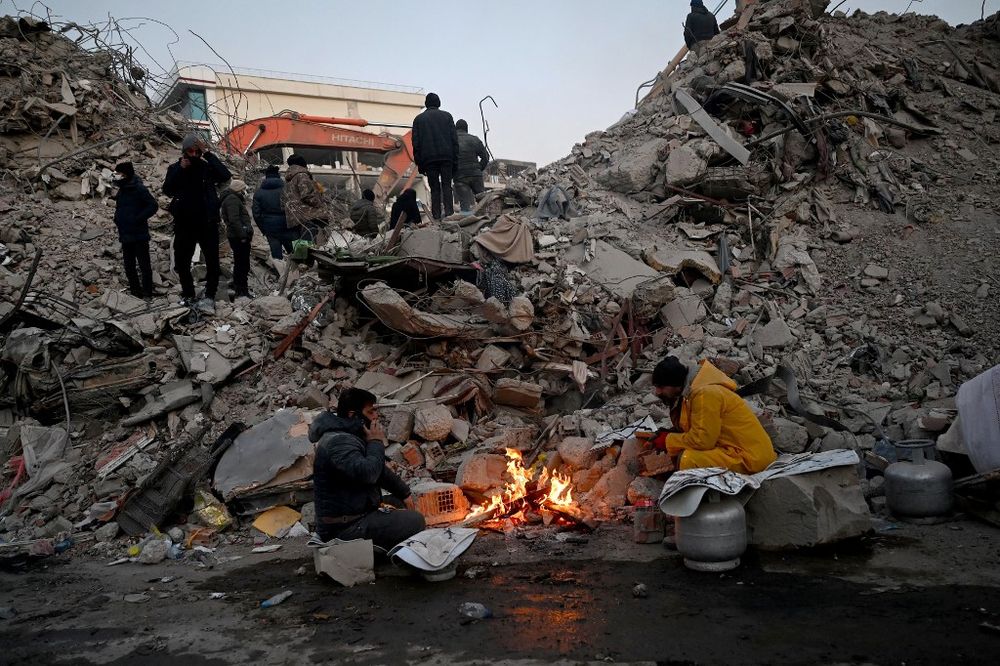 Survivors warm up around a fire in front of collapsed building rubble as rescue teams search for victims, in Turkey.