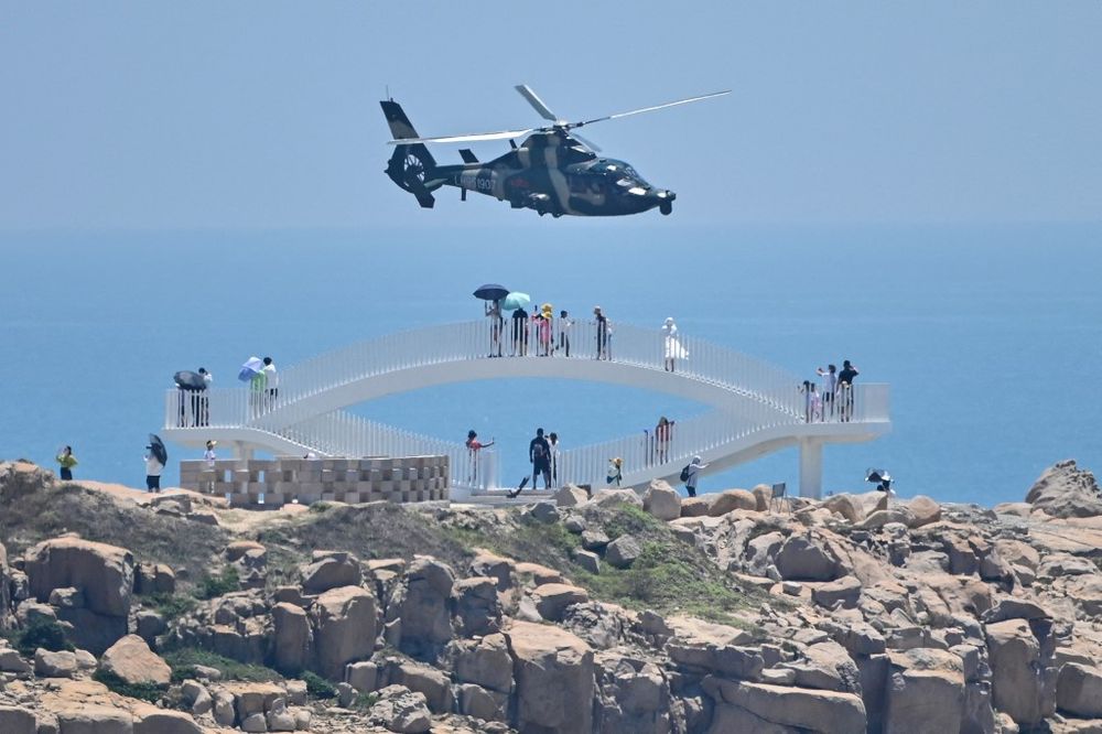 Tourists look on as a Chinese military helicopter flies past Pingtan island, one of mainland China's closest points from Taiwan, in Fujian province, China, on August 4, 2022