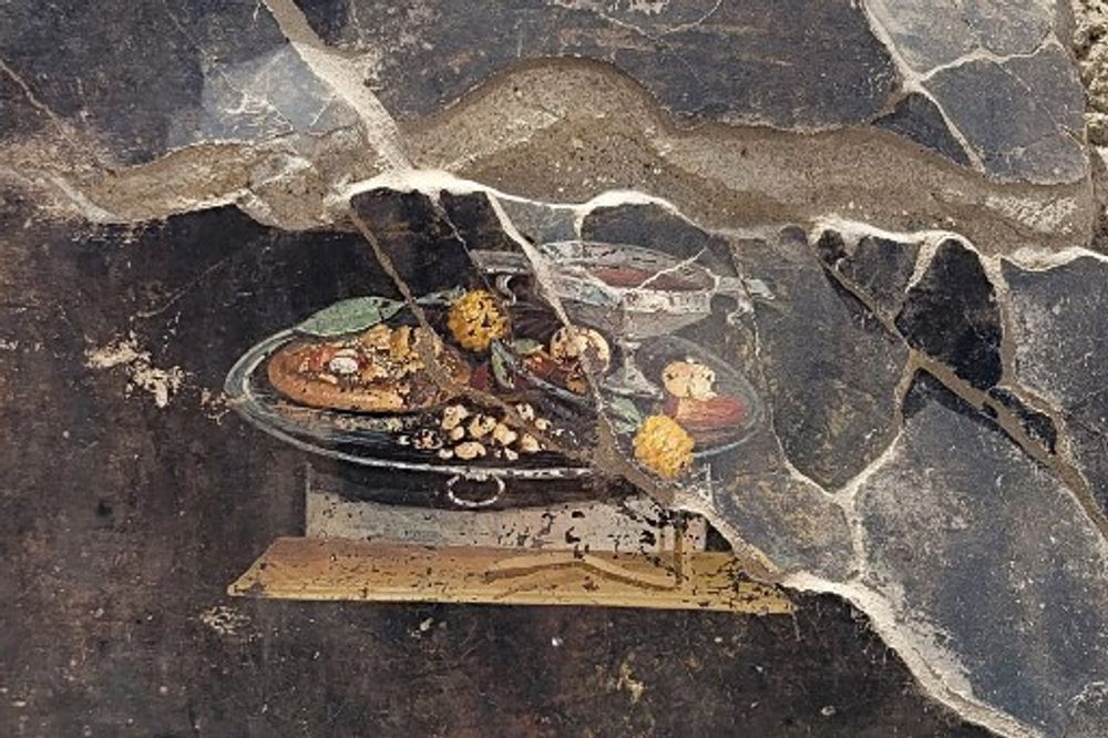 This handout photo taken and released by the Archaeological Park of Pompeii, shows a 2,000-year-old Pompeian painting, found by the new Regio IX excavations, on the wall of an ancient house that could be a distant ancestor of modern pizza.