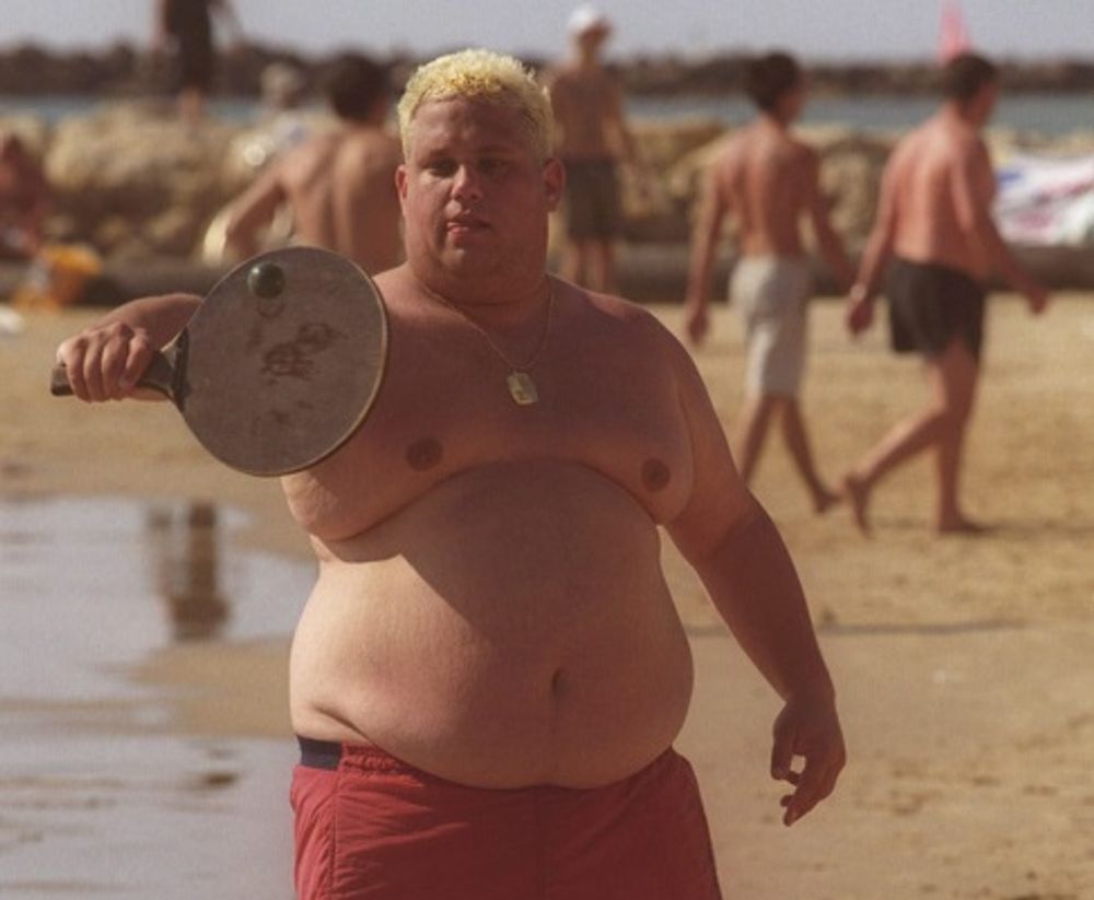 An overweight Israeli man plays paddle ball at the beach in Tel Aviv.