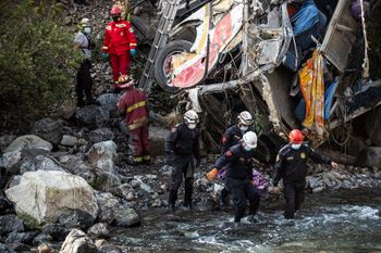 Rescue workers and police officers retrieve a body from a bus that crashed in the Andes Mountains, Peru