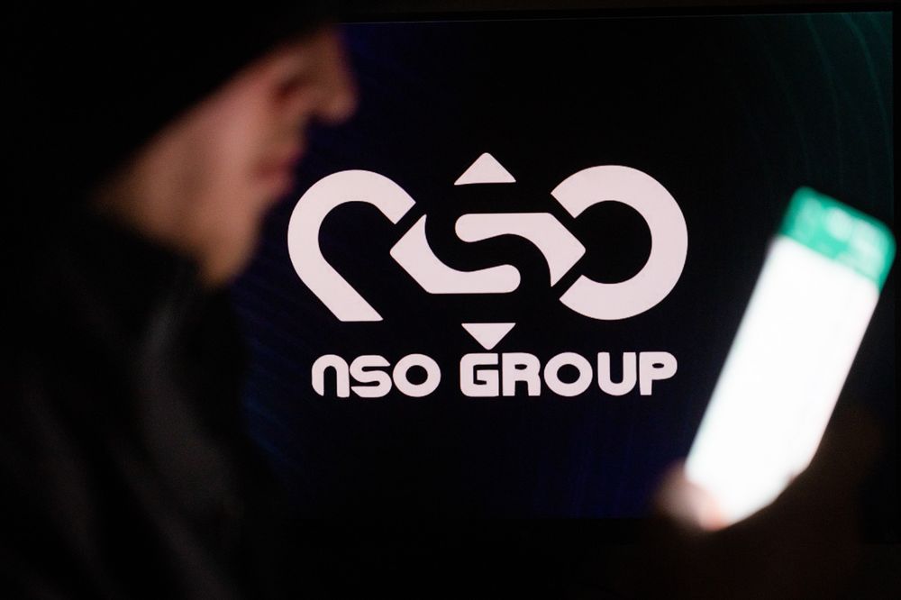 Illustration - un homme tient son téléphone avec le logo NSO GROUP sur un écran d'ordinateur à l'arrière-plan, à Jérusalem, le 7 février 2022