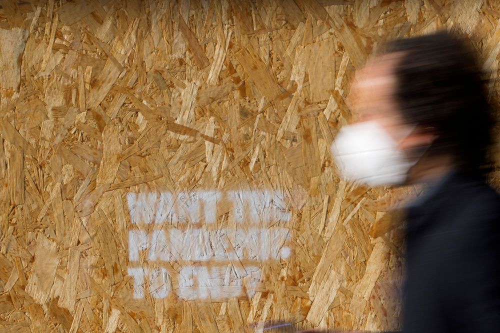 A man wearing a face mask walks past a wooden board with graffiti reading "Want the pandemic to end?" in Rome, January 7, 2022.
