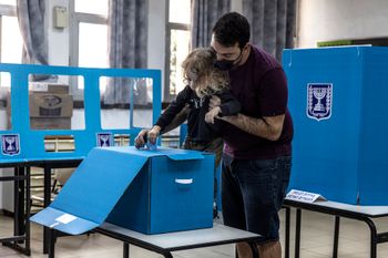 An Israeli guides his child in casting the ballot for Israel's parliamentary election at a polling station in the city of Yavne, Israel, on March 23, 2021.