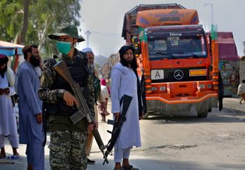 A Pakistani paramilitary soldier (L) and Afghan Taliban fighters stand guard on their respective sides at a border crossing point in Torkham, Pakistan.