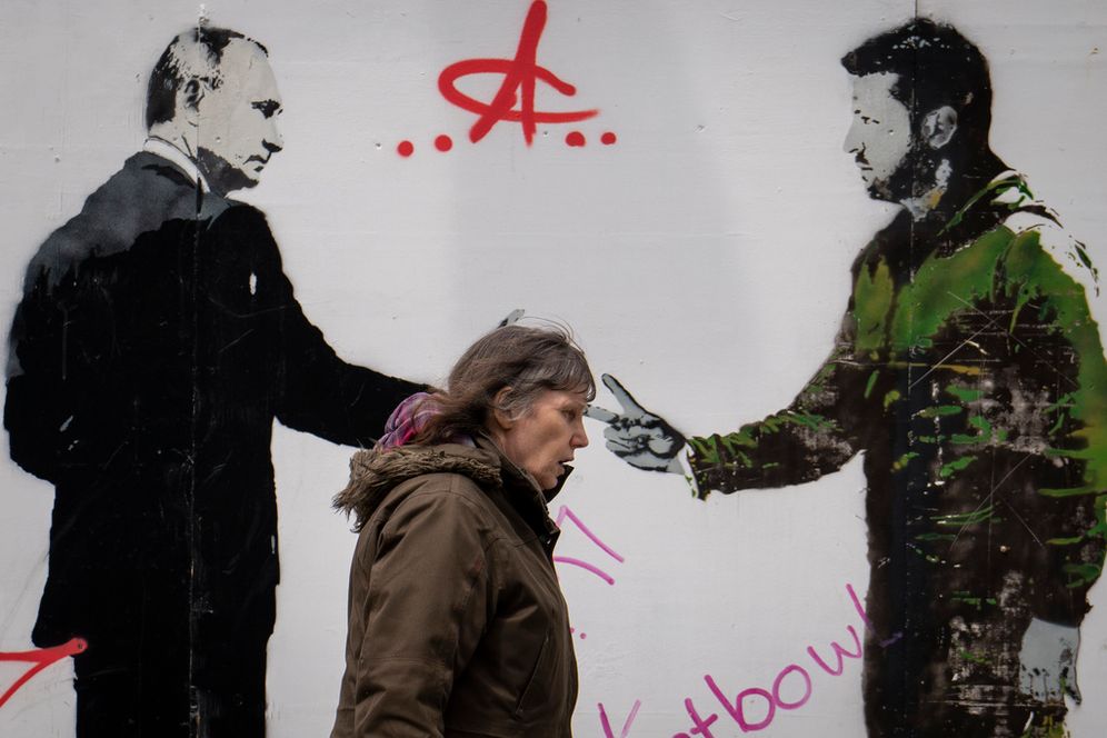 A woman walks by graffiti depicting Ukrainian President Volodymyr Zelenskyy (R) and Russian leader Vladimir Putin in London, England.