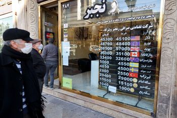 Men look at at currency exchange rates posted by an exchange shop in Tehran, Iran.