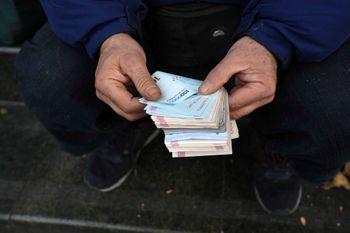 A street money exchanger poses for a photo without showing his face as he counts Iranian banknotes at a commercial district in downtown Tehran, Iran, Friday, Dec. 23, 2022.
