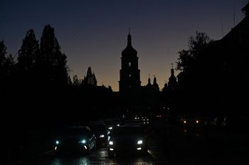 Vehicles drive along a street with the St. Sophia Cathedral silhouetted in the background, as the city is plunged into near darkness following a military strike that partially brought down the power infrastructure, in Kyiv, Ukraine.