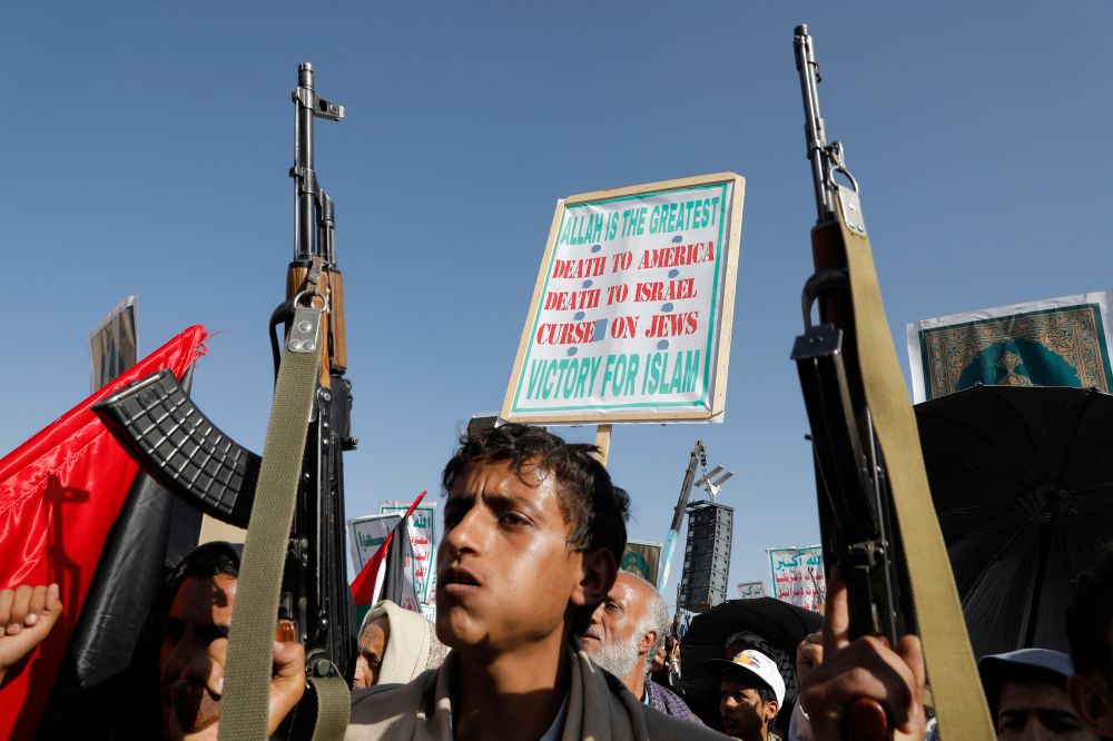 Houthis demonstrating in Yemen, with their flag translated into English 