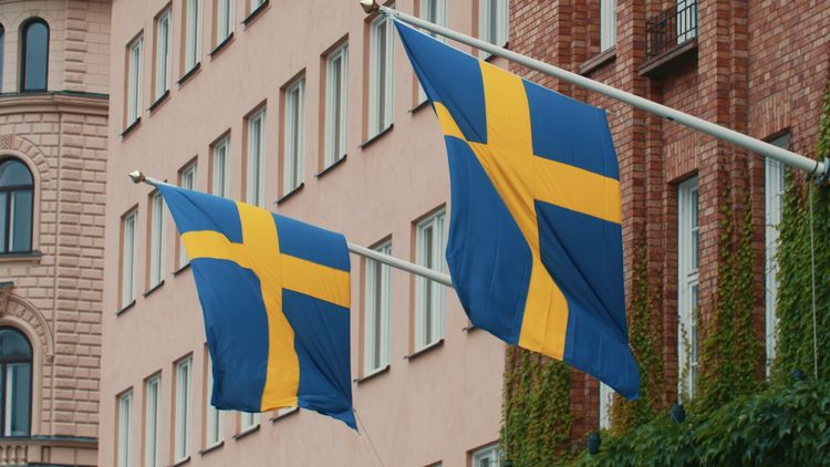 Still image of two Swedish flags waving on poles on the building on a windy day