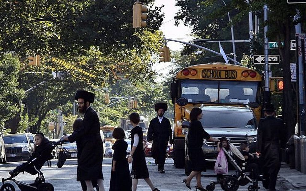 Children and adults cross a street in front of a school bus in Borough Park, a neighborhood in the Brooklyn borough of New York that is home to many ultra-Orthodox Jewish families.