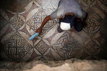 A Palestinian sweeps dust off parts of a Byzantine-era mosaic floor that was uncovered by a farmer in Bureij in the central Gaza Strip, on September 5, 2022.