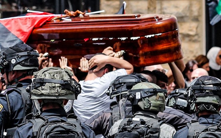 Amro Abu Khudeir (gray shirt) covers his head protectively as he carries the casket of slain Al-Jazeera journalist Shireen Abu Akleh out of a hospital, before being transported to a church and then her resting place, in Jerusalem, May 13, 2022.