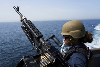 A U.S. Navy retail service specialist stands guard next to a machine gun aboard the USS Paul Hamilton in the Strait of Hormuz.