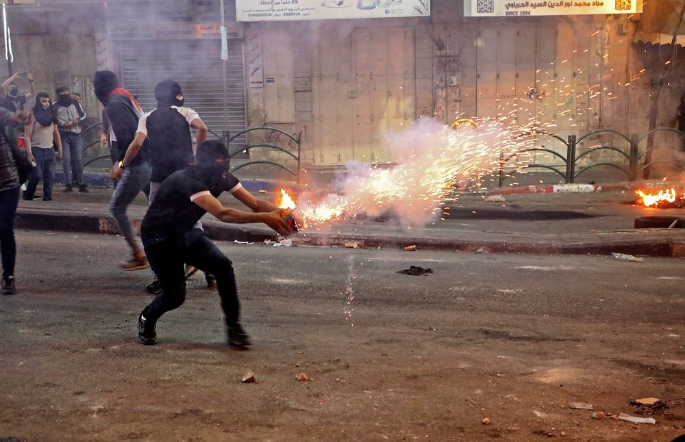 Un manifestant palestinien lance des fusées éclairantes au milieu d'affrontements avec des soldats israéliens dans le centre-ville d'Hébron en Cisjordanie, le 14 mai 2021
