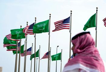 رجل يقف تحت العلمين الأمريكي والسعودي قبل زيارة الرئيس الأمريكي جو بايدن، في ساحة في جدة، المملكة العربية السعودية، الخميس 14 يوليو 2022.
