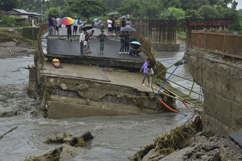 People stand on a damaged bridge over the Daranga River after flash floods washed away a section of the bridge following monsoon rains in Kumarikata village of Baska district, in India's Assam state.