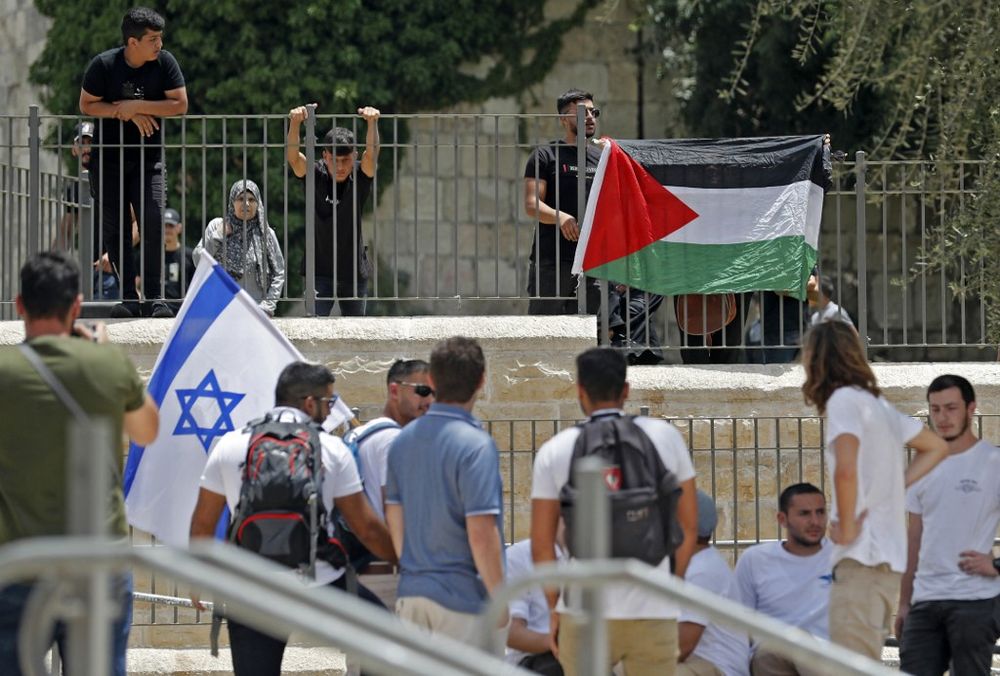 Palestinian protesters lift their national flag on a fence across from Israelis lifting theirs at Jerusalem's Damascus Gate, as Israelis mark Jerusalem Day, on May 29, 2022.