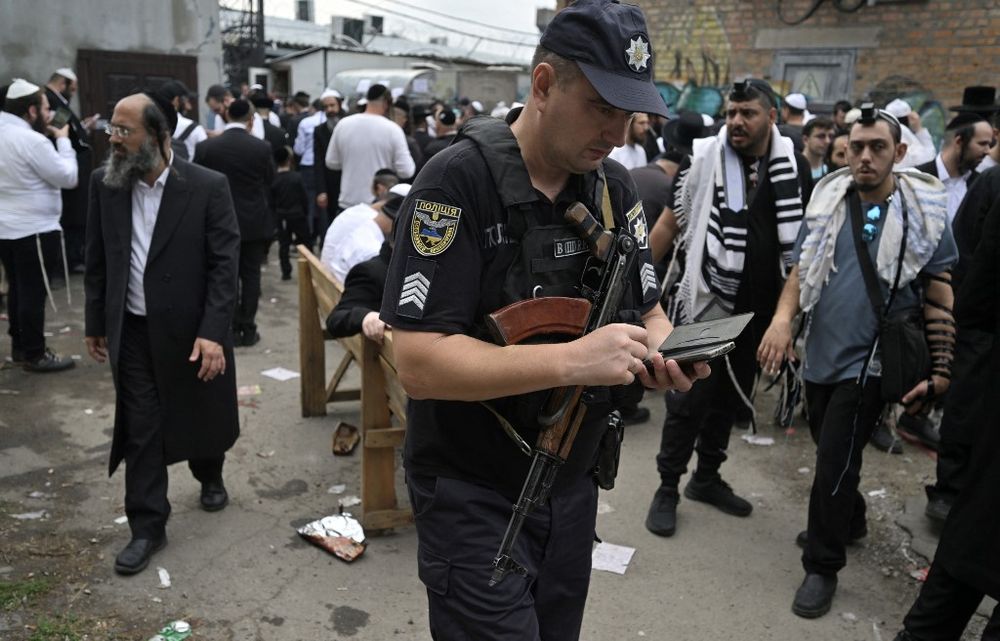 Un policier ukrainien sur son smartphone alors que des pèlerins juifs hassidiques marchent dans une rue près de la tombe de Rabbi Nahman